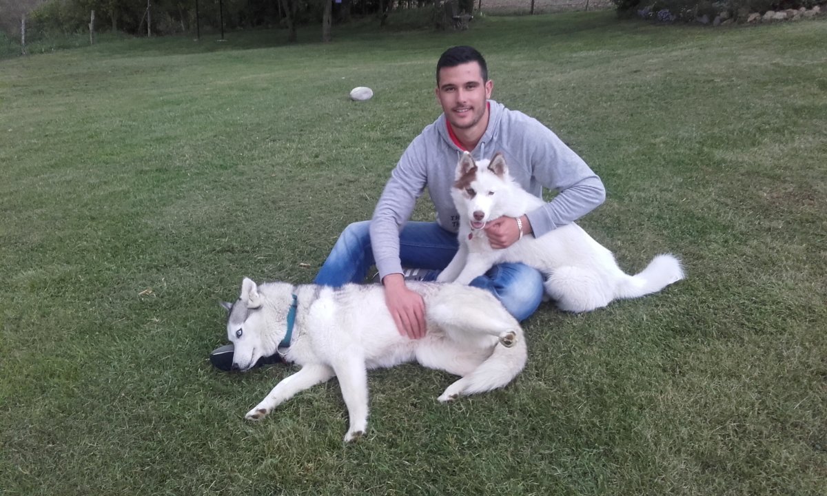 "Photographie en extérieur d'un homme complice assis avec deux Huskys (un adulte et un chiot), illustrant l'apprentissage par le plaisir."