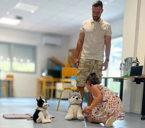 intervenant-peccram-exercice-peluche-pédagogique-enfant-caniviola Un intervenant PECCRAM supervise une petite fille s'exerçant aux bons gestes d'approche avec une peluche pédagogique posée au sol.
